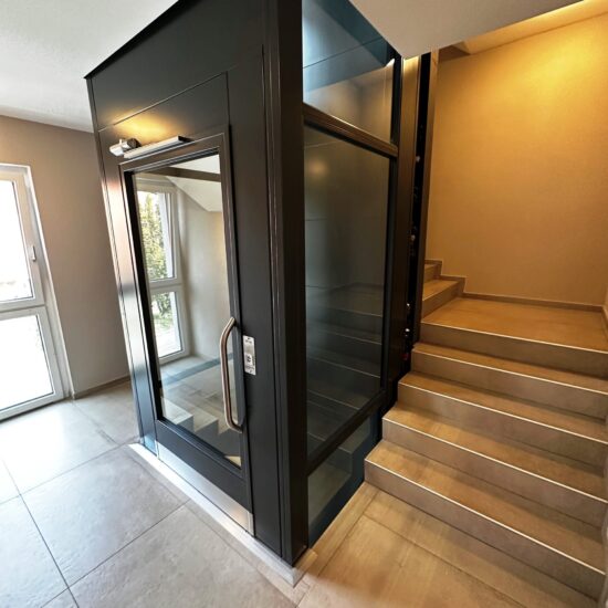 Homelift Plattformlift im Treppenauge von einem Mehrfamilienhaus mit grossem Glas